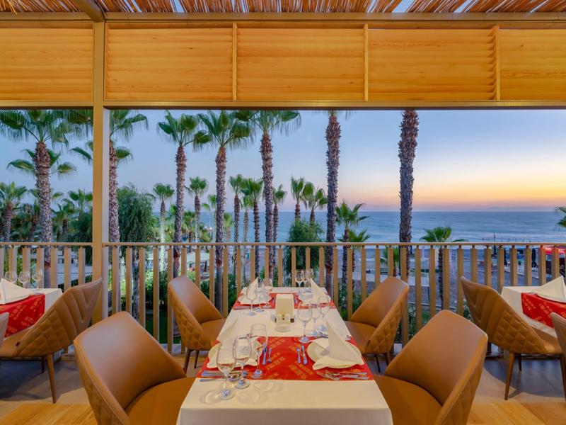 Terasa s prostřenými stoly s výhledem na palmy a moře při západu slunce.