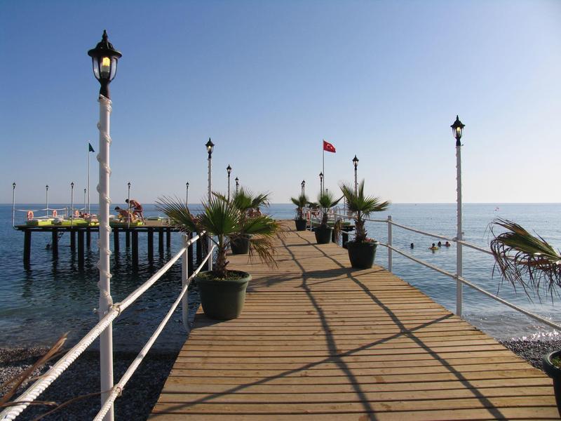 Dřevěný mol vede přes moře, obklopené lampami a květináči s rostlinami.