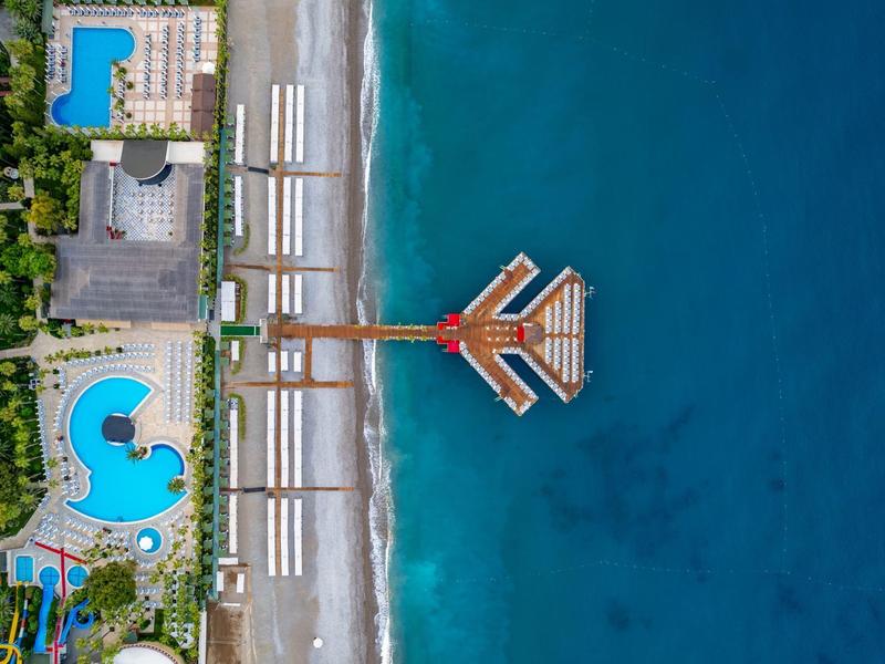 Aerial view of a hotel with pools, wooden pier, and beach by the blue sea.