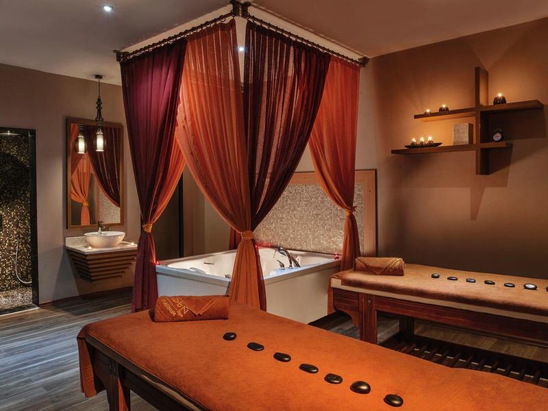 Cozy spa room with massage tables and a whirlpool bathtub draped with curtains.
