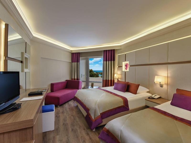 Modern hotel room with two beds and purple accents, window overlooking trees.
