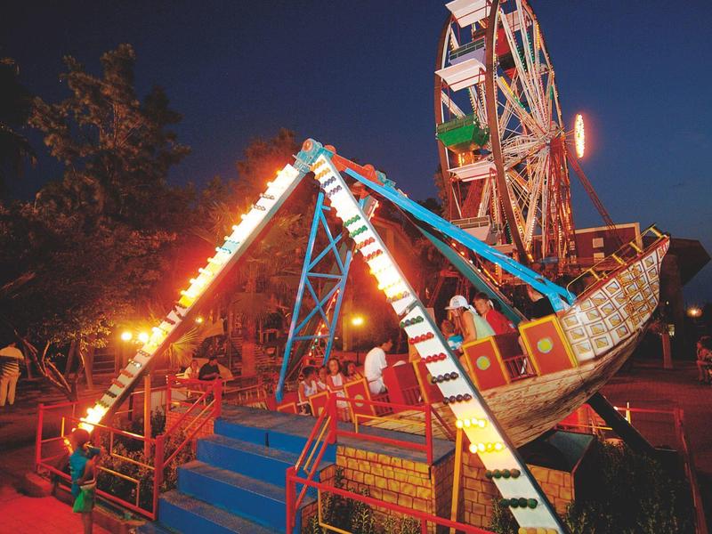 Illuminated Ferris wheel and Viking ship carousel at night on a fairground.