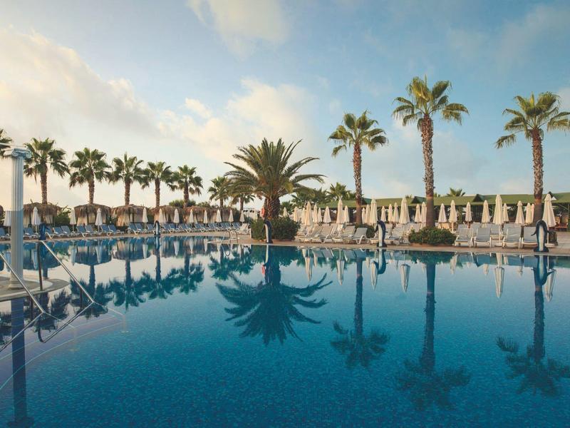 Large hotel pool with palm trees and lounge chairs under a blue sky.