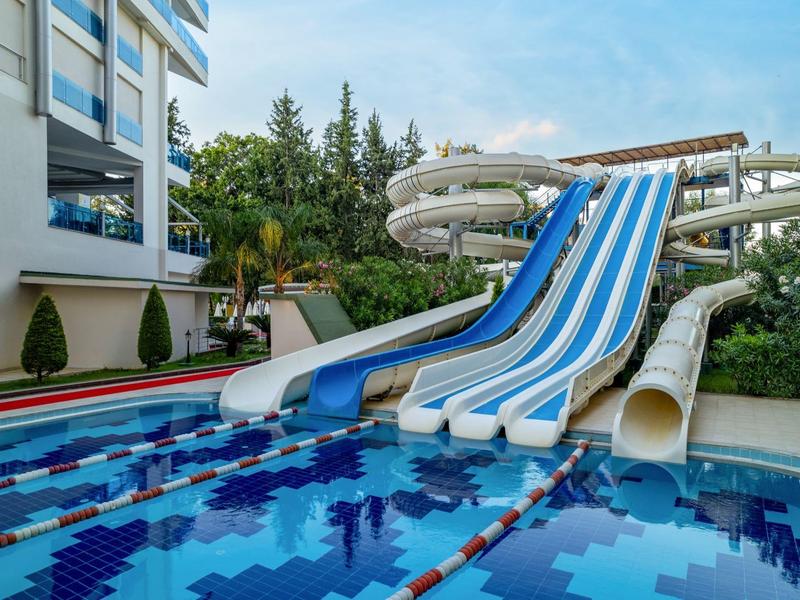 Water slides next to a pool beside a hotel building with surrounding vegetation.