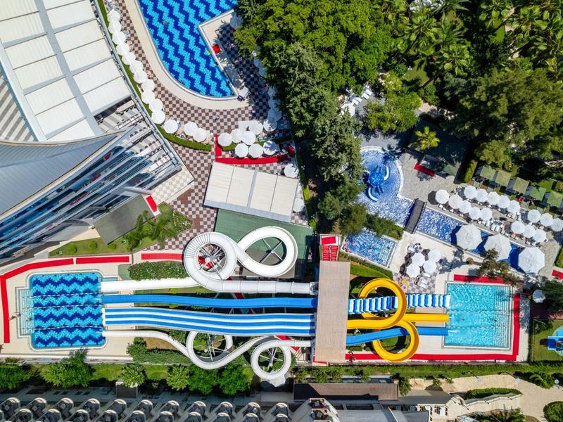 Aerial view of a water park featuring water slides, pools, and sun umbrellas surrounded by greenery.