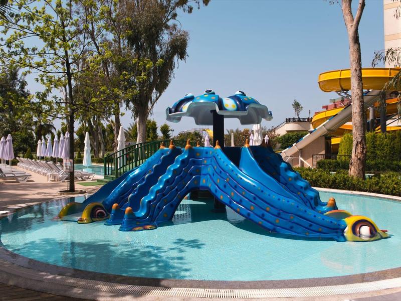 Small water park with blue water slides and splash pool under clear sky.