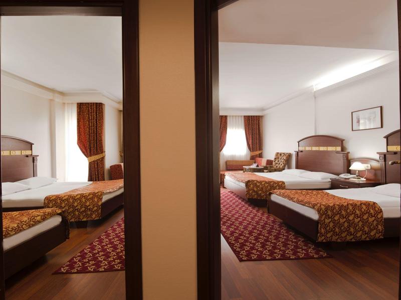 Two adjoining hotel rooms with beds, rugs, and curtains, separated by a wall.