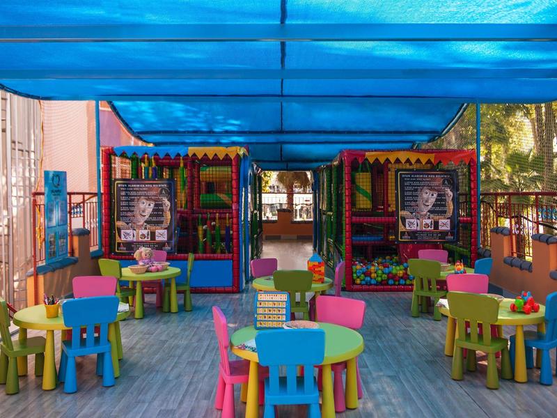 Colorful outdoor area with kids' tables and chairs under blue canopy at a hotel.