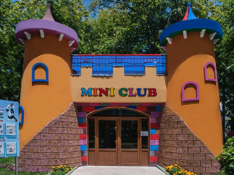 Colorful building with towers and a 'Mini Club' sign in a wooded area.