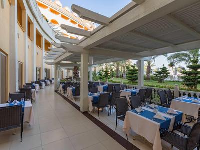 Terrazza esterna di un ristorante d'hotel con tavoli e sedie sotto pergolato e vista sul giardino.