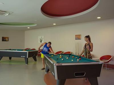 Dos personas juegan al billar en una sala moderna con acentos redondos de color en el techo.