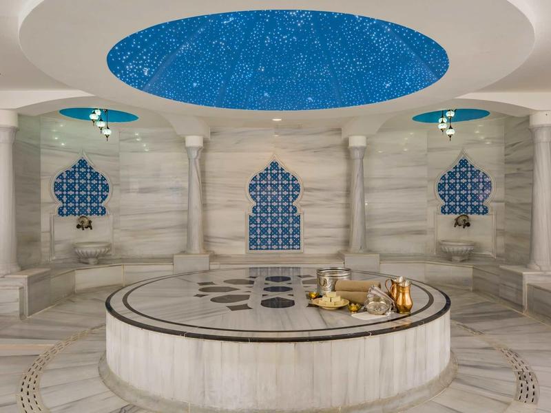 Interno di un hammam lussuoso con soffitto blu stellato e fontana centrale in marmo.