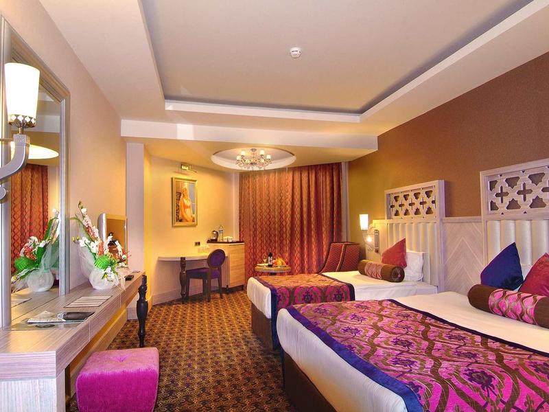 Elegante camera d'hotel con letti matrimoniali, mobili in legno chiaro e decorazioni viola.