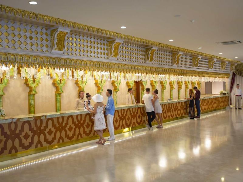 Reception di un hotel luminosa con decorazioni floreali e clienti al banco.