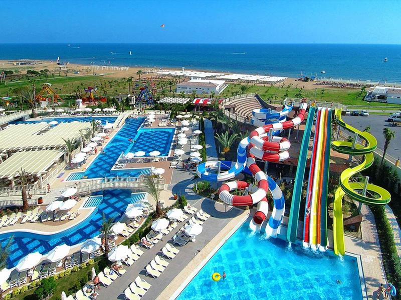 Grande parco acquatico sul mare con piscine, scivoli colorati e lettini.