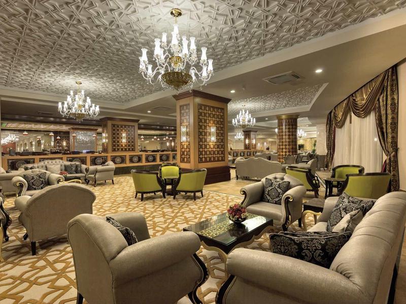 Ampia sala d'albergo con poltrone, tappeto beige, lampadari eleganti e arredamento classico.