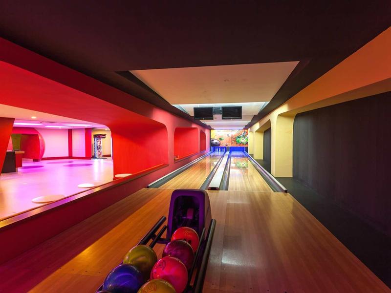 Corsia da bowling moderna con pareti rosse e gialle, palle colorate e illuminazione soffusa.