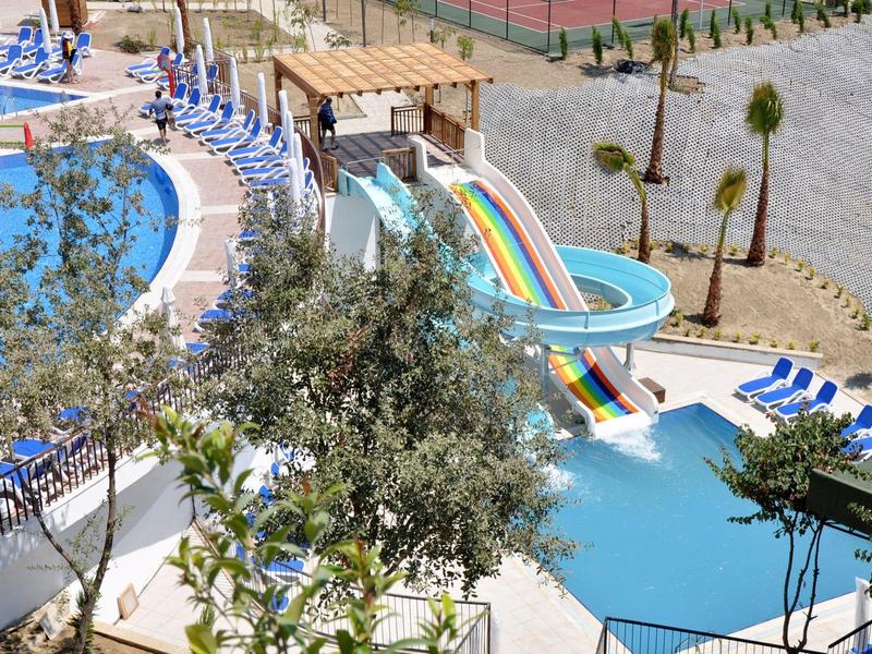 Scivolo d'acqua colorato nella zona piscina con sdraio e palme.