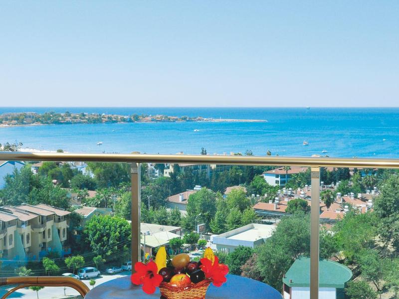 Tavolo sul balcone con bevande e vista mare, palme e edifici sullo sfondo.
