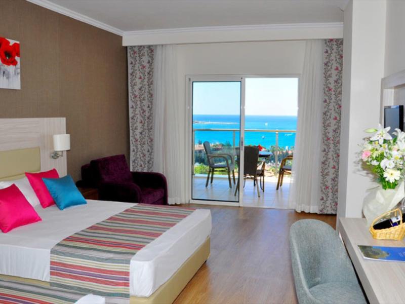 Camera d'hotel moderna con letto matrimoniale, cuscini colorati, balcone e vista mare.