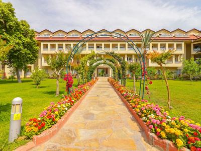 Blick auf einen begehbaren Weg mit Blumenbeeten und einem Hotelgebäude im Hintergrund.