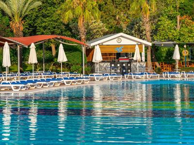 Grande piscina all'aperto con lettini, ombrelloni e vegetazione tropicale sullo sfondo.