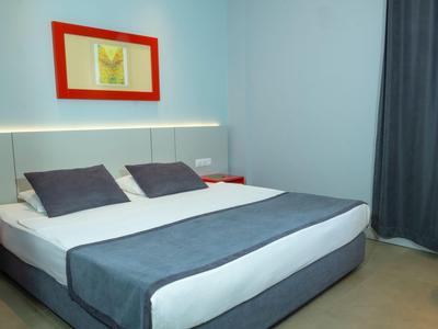 Modernes Hotelzimmer mit großem Bett, grauer und weißer Bettwäsche und rotem Wandbild.