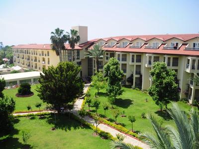 Großes Hotelgebäude mit rotem Dach und grünen Gärten unter blauem Himmel.