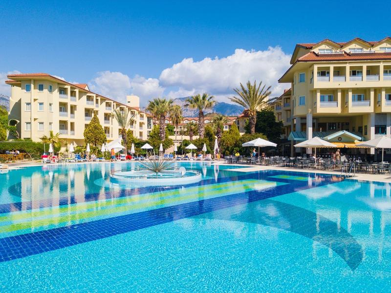 Grande piscina dell'hotel con lettini, ombrelloni e palme sotto un cielo azzurro.