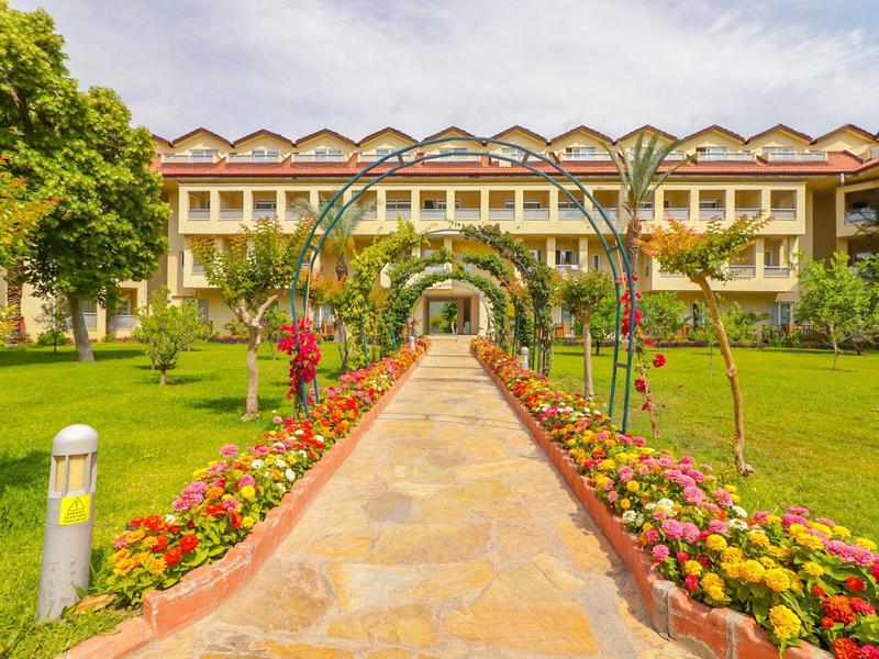 Sentiero attraverso un giardino fiorito che conduce a un edificio di hotel su più piani sotto un cielo nuvoloso.