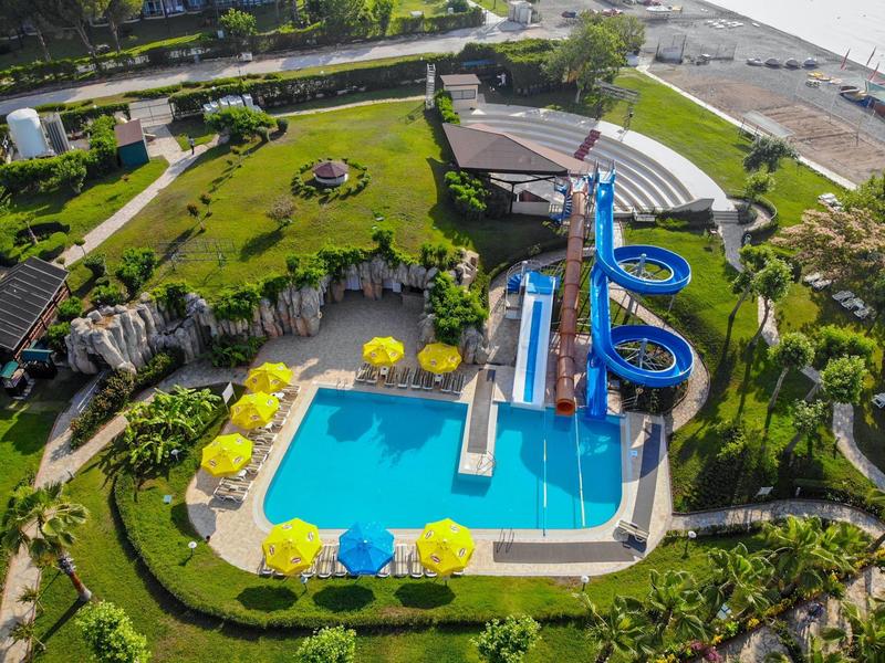 Vista di una piscina all'aperto con scivoli d'acqua e ombrelloni accanto a un giardino verde e al mare.
