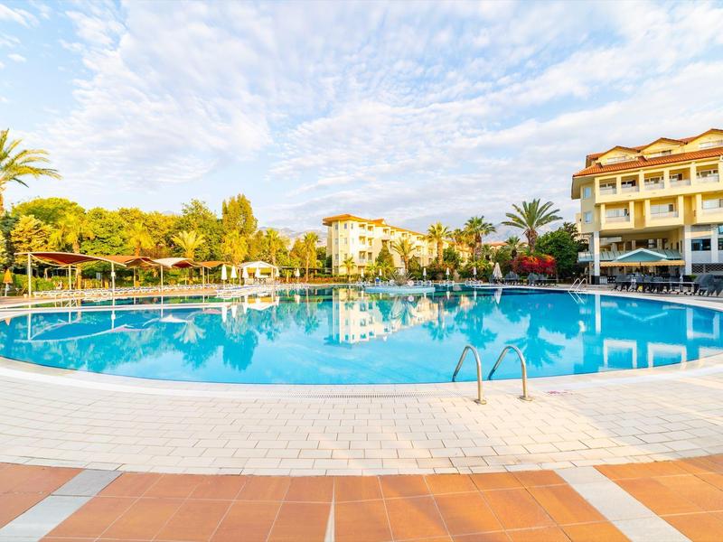 Grande piscina rotonda in un complesso alberghiero con palme e edifici a più piani sullo sfondo.