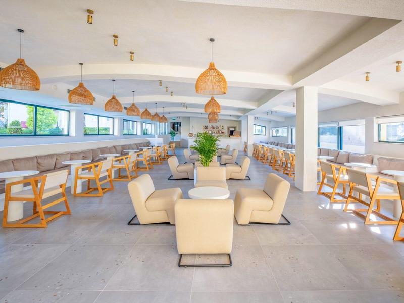 Lounge hotel moderno e luminoso con poltrone confortevoli e tavoli in legno, decorato con piante.