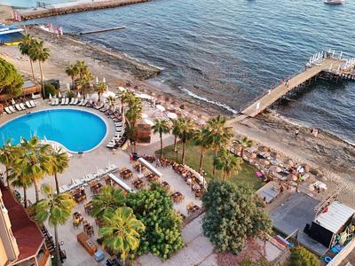 Uitzicht op een zwembad, strand en pier bij een kustresort in zonlicht.