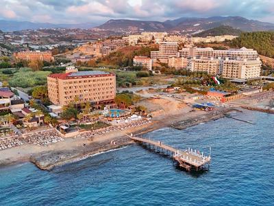 Kustplaats met strand, ligstoelen en pier aan zee met bergen op de achtergrond.