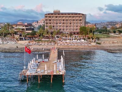 Uitzicht op een hotelsteiger met ligstoelen en een groot hotelgebouw op de achtergrond aan de kust.