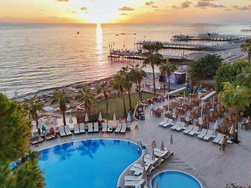 Hotelzwembad met ligstoelen en uitzicht op zee bij zonsondergang.
