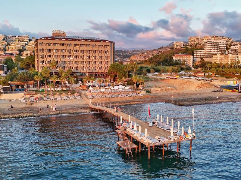 Hotel met zandstrand, steiger en ligstoelen bij kustplaats bij zonsondergang.