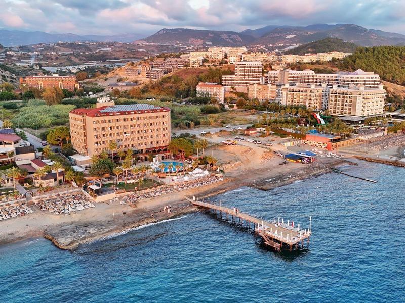 Kustplaats met strand, ligstoelen en pier aan zee met bergen op de achtergrond.