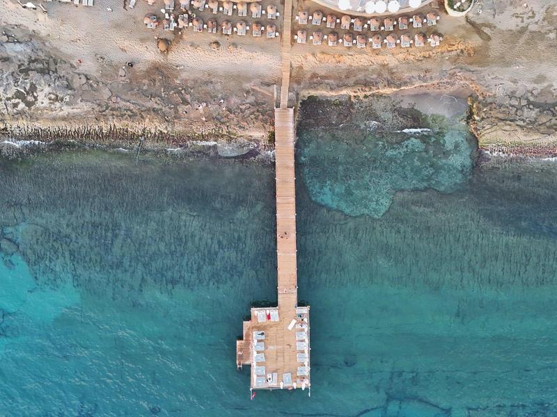 Luchtfoto van een houten pier die zich uitstrekt in helderblauw kustwater.