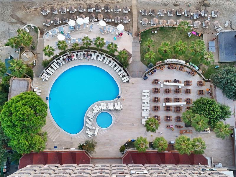 Luchtfoto van een hotelentree met een blauw zwembad, ligbedden en een aangrenzend zandgebied.