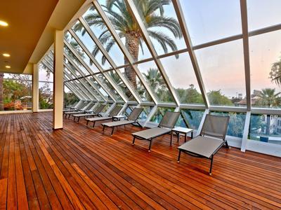 Terrazza coperta con lettini e vista su palme e acqua al tramonto.