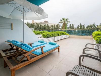 Grande terrasse avec piscine, chaises longues et chaises, entourée de verdure et vue sur l'hôtel.
