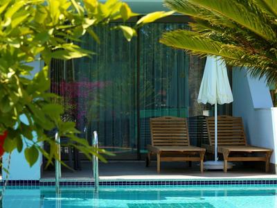 Piscine d'hôtel avec deux chaises longues, un parasol et des plantes vertes luxuriantes autour.