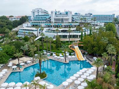 Hotel di lusso con grande piscina, scivolo d'acqua e numerosi lettini circondati da verde.
