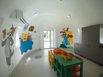 Camera per bambini luminosa con tavoli e sedie colorati e murales di cartoni animati.