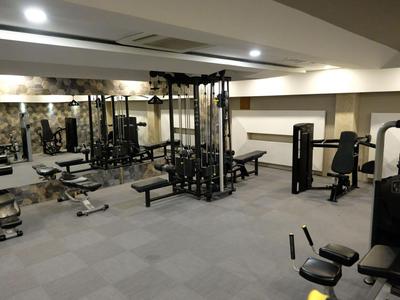 Une salle de sport moderne avec divers appareils de musculation et bancs de poids sur un sol en moquette grise.