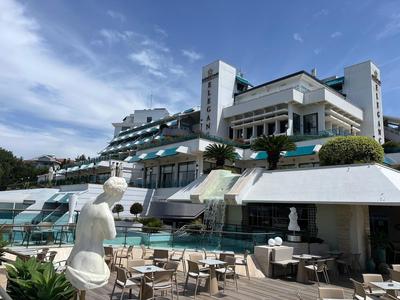 Hotel moderno con terrazza, tavoli e statue sotto un cielo blu.