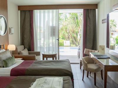 Chambre d'hôtel avec deux lits, coin salon et vue sur terrasse avec jardin.