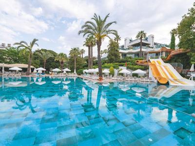 Grande piscine d'hôtel bleue avec toboggans, transats et palmiers sous un ciel nuageux.